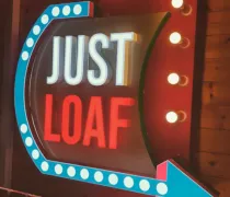 A brightly lit sign featuring the words 'JUST LOAF,' with colorful borders and lights