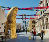 A large golden sculpture resembling a hand stands in an open marketplace, with colorful flags strung above