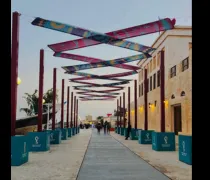 A scenic walkway lined with colorful banners and illuminated buildings, bustling with people in a festive atmosphere