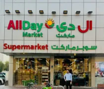 The exterior of an AllDay Market supermarket features bright signage in English and Arabic, with a man standing by bicycles
