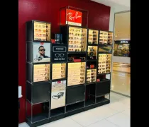 A sunglasses display rack featuring various Ray-Ban styles, accompanied by promotional images, against a red wall