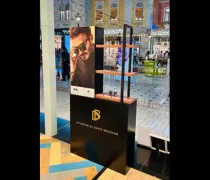 A sleek promotional display features a model wearing sunglasses, set in a vibrant shopping space with shelves