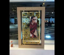 A stylish display featuring a woman in sunglasses and a red scarf, framed by a decorative golden border, labeled 'Bvlgari'