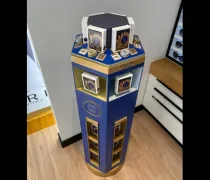 A cylindrical display stand with blue and gold accents showcases various products in square boxes and circular containers
