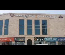 A stone building featuring large windows, displaying signs for 'Fitness Extreme' and other businesses in Arabic and English
