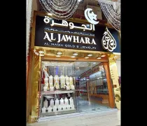 The storefront of Al Jawhara jewelry shop features elegant gold displays, illuminated signage, and decorative accents