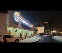 A well-lit City Exchange building at night, with an illuminated sign and a few people near the entrance, surrounded by modern buildings