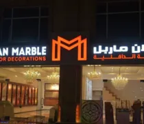 A well-lit storefront featuring  Iran Marble  sign in English and Arabic, showcasing marble decor with ornate chandeliers inside