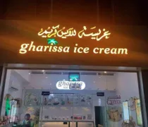 The storefront of Gharissa Ice Cream features a warm-lit sign in Arabic and English, welcoming customers to enjoy treats