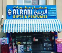 A shopfront featuring a blue and yellow striped awning with 'Al Rabi Gifts & Perfumes' prominently displayed above