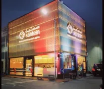 A modern building facade at night, featuring colorful lighting and the 'Sahtein' logo prominently displayed